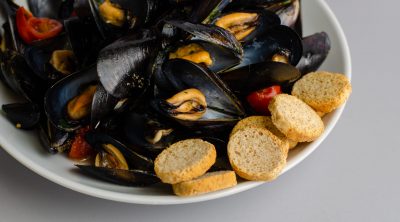Close up shot of steamed mussel soup with crisp bread and tomatoes. Mediterranean food concept.